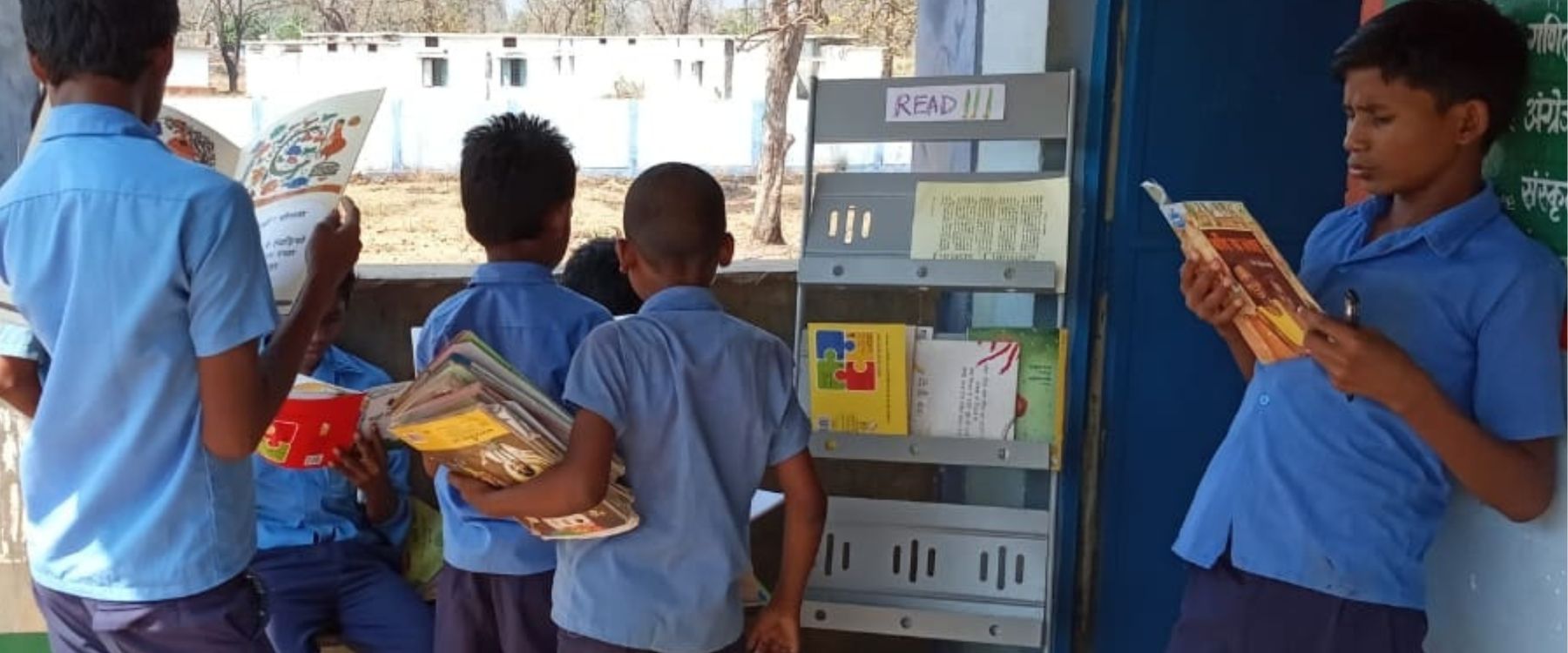 Children reading books outside a classroom in a government school