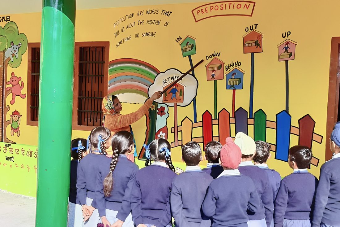 A teacher using a painted classroom wall to teach prepositions