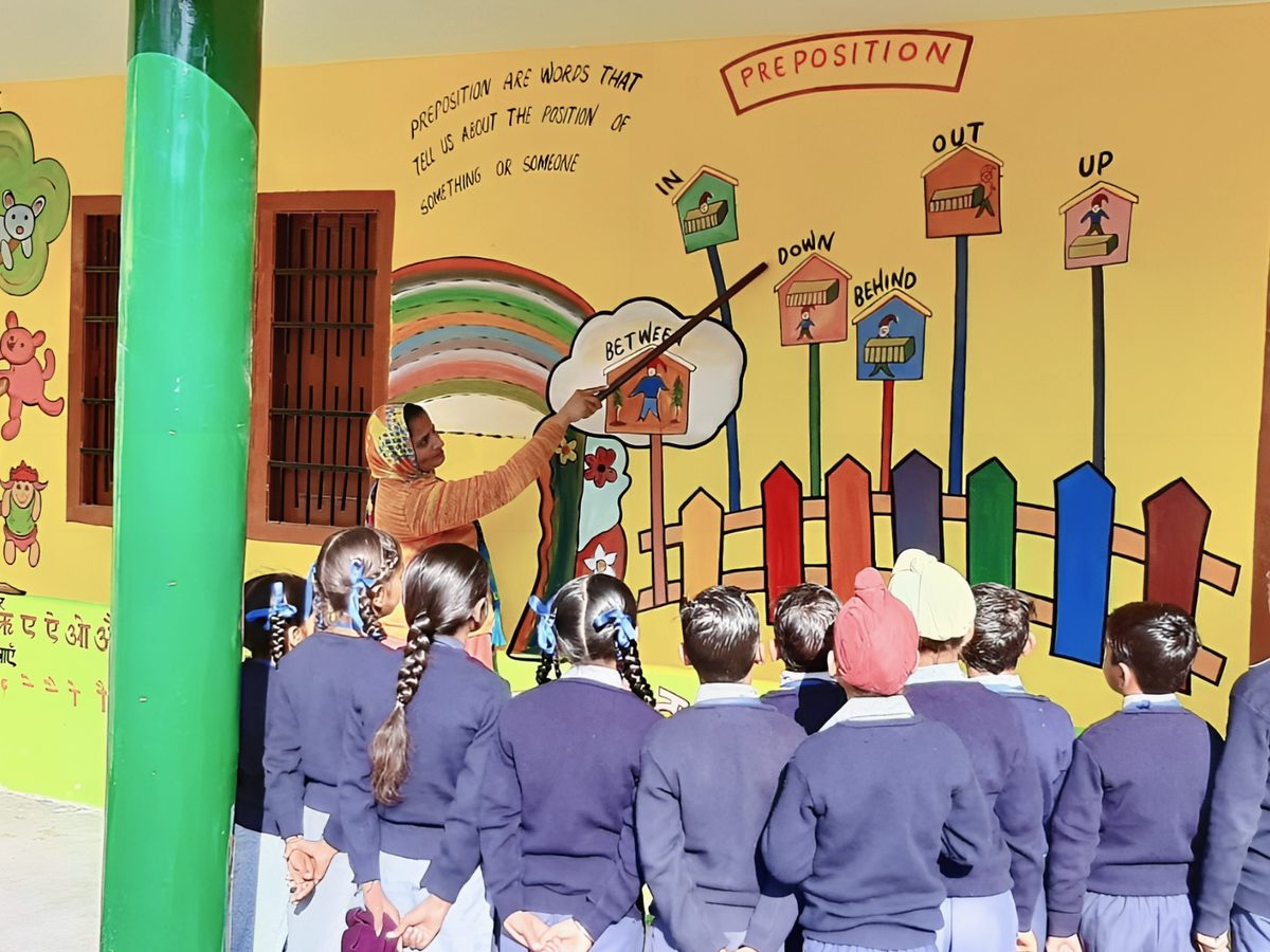 A teacher using a painted classroom wall to teach prepositions